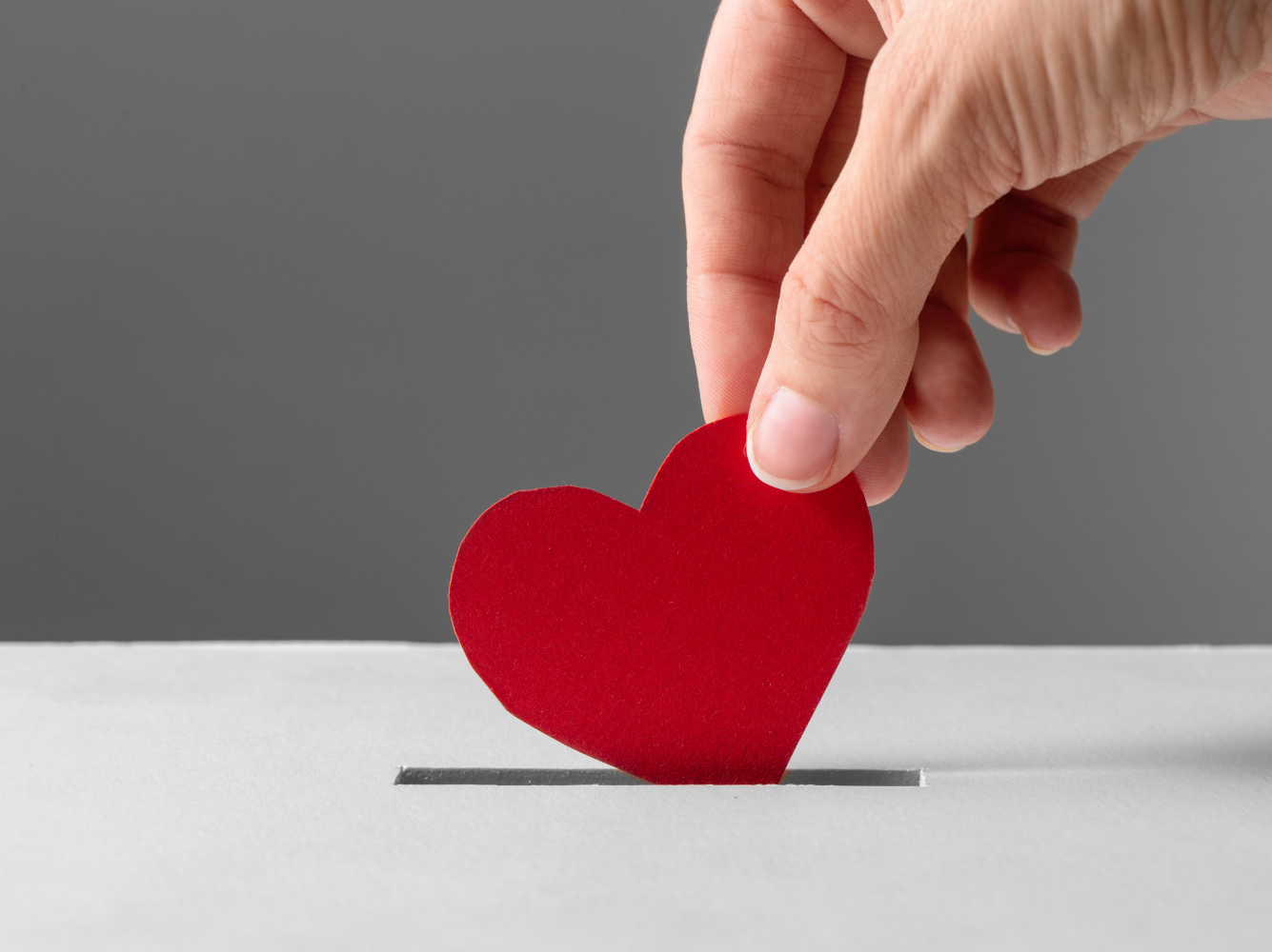 A hand placing a paper heart into a donation box, symbolizing support for charitable contributions. Accompanied by the blog title 'How Nonprofit Organizations Use Marketing.